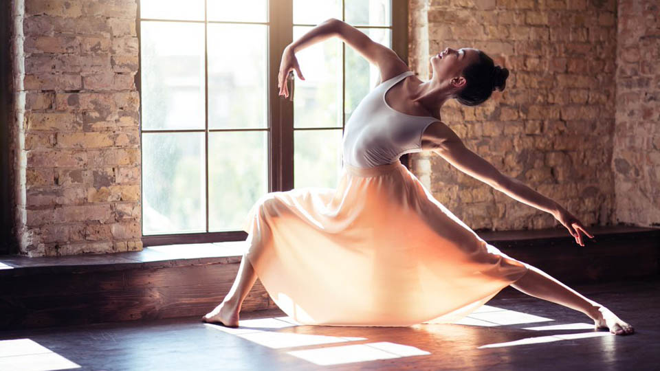 A ballet dancer strikes a pose, backlit in front of a window
